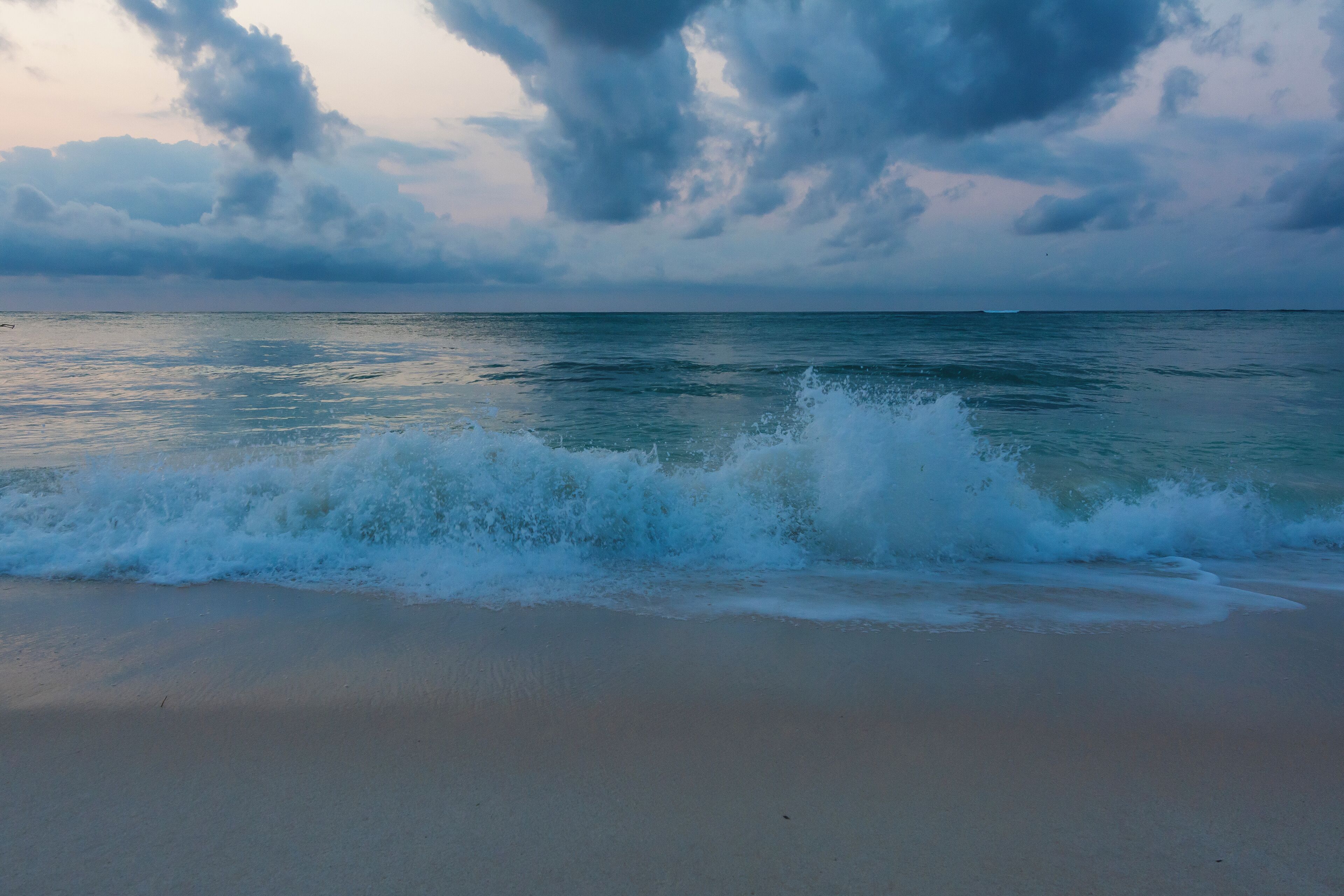A beach with waves crashing onto the shore under a cloudy sky.