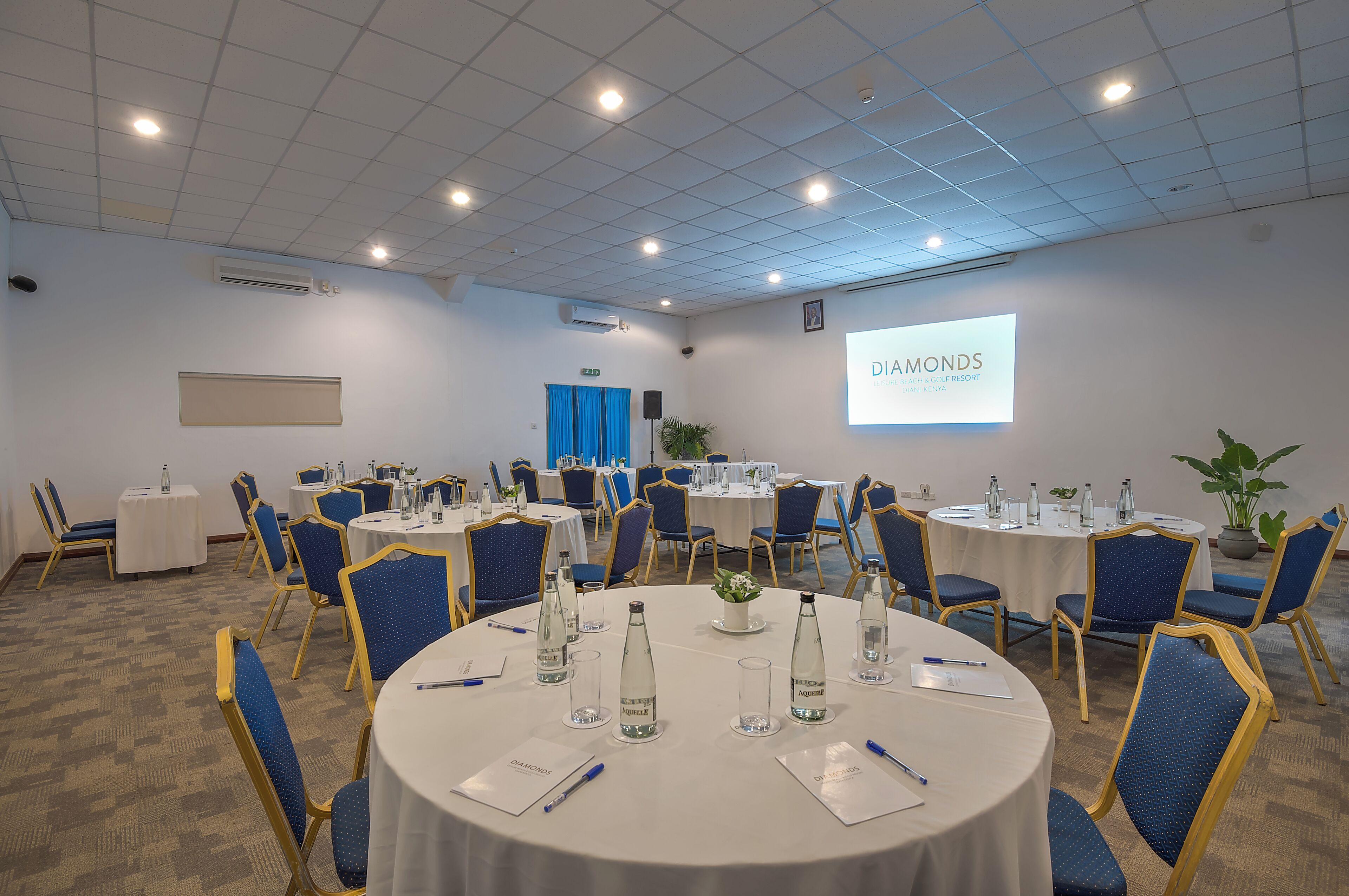 Un salón de conferencias con mesas redondas, sillas azules y manteles blancos.
