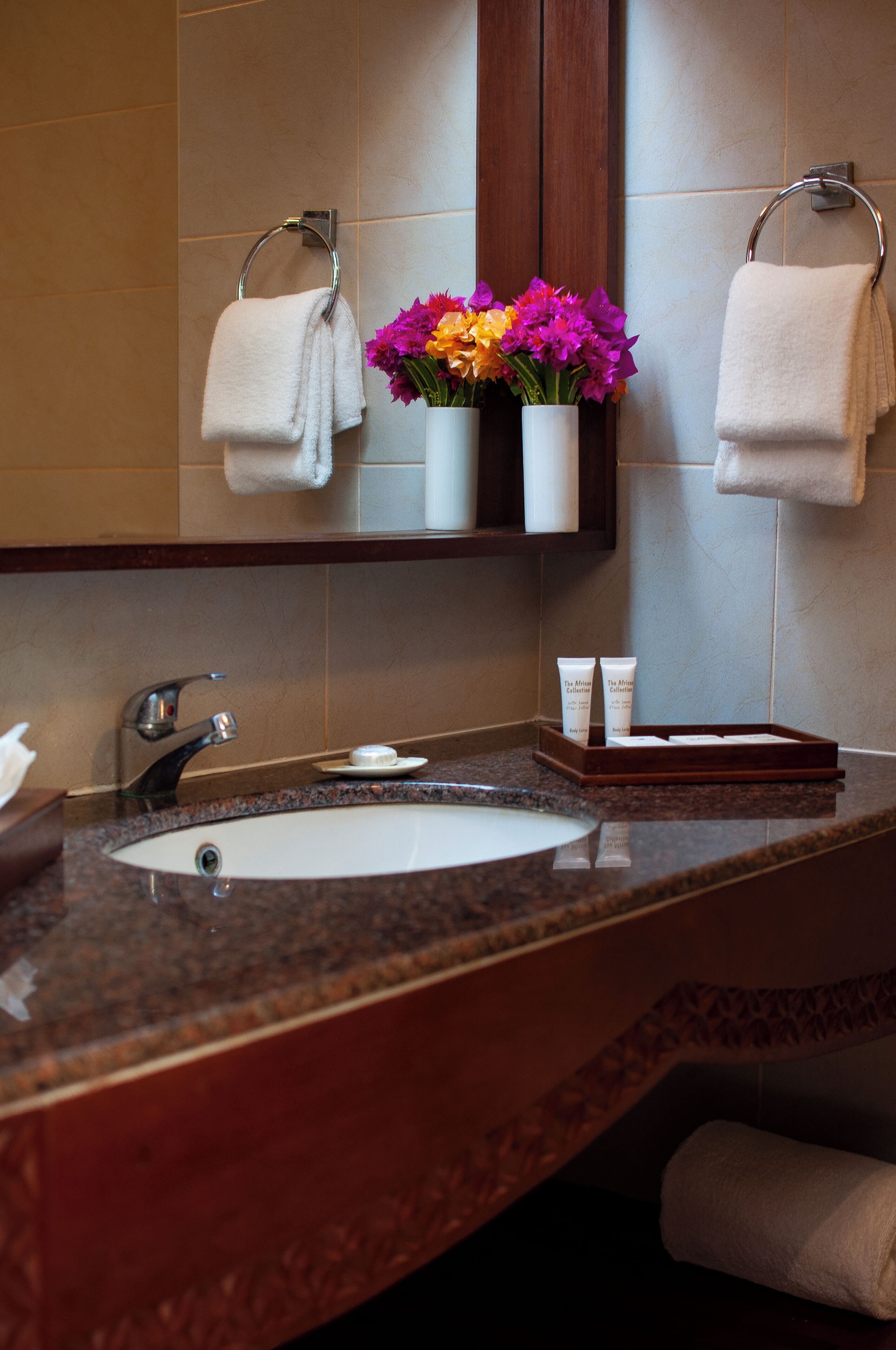 A bathroom with a marble sink, two towels, a mirror, and a vase with flowers.