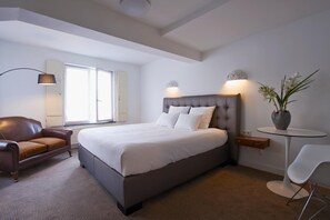 Une chambre d’hôtel moderne avec un grand lit, un canapé en cuir, une petite table ronde et une plante en pot.