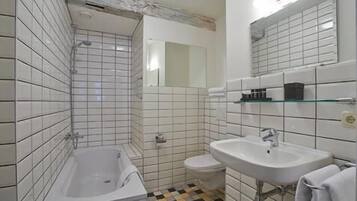 A bathroom with white tiled walls, a white bathtub, a white sink, and a toilet.