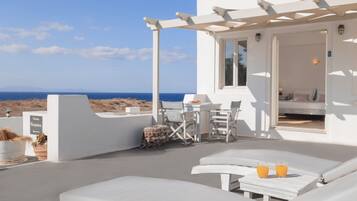 Zona relax esterna con sedie a sdraio e tavolo, con vista sul mare.