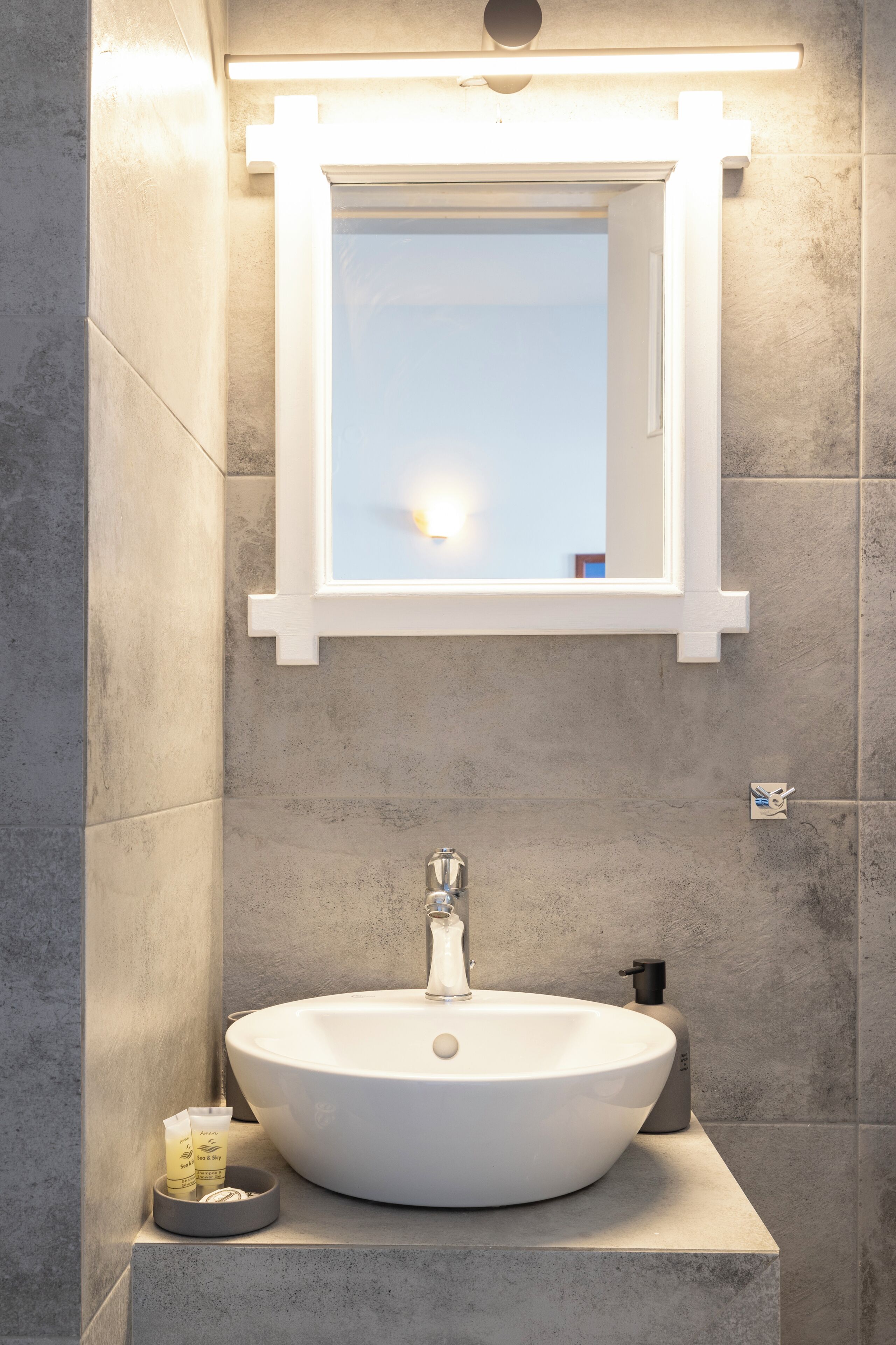 A bathroom with a white sink, a mirror, and a soap dispenser.