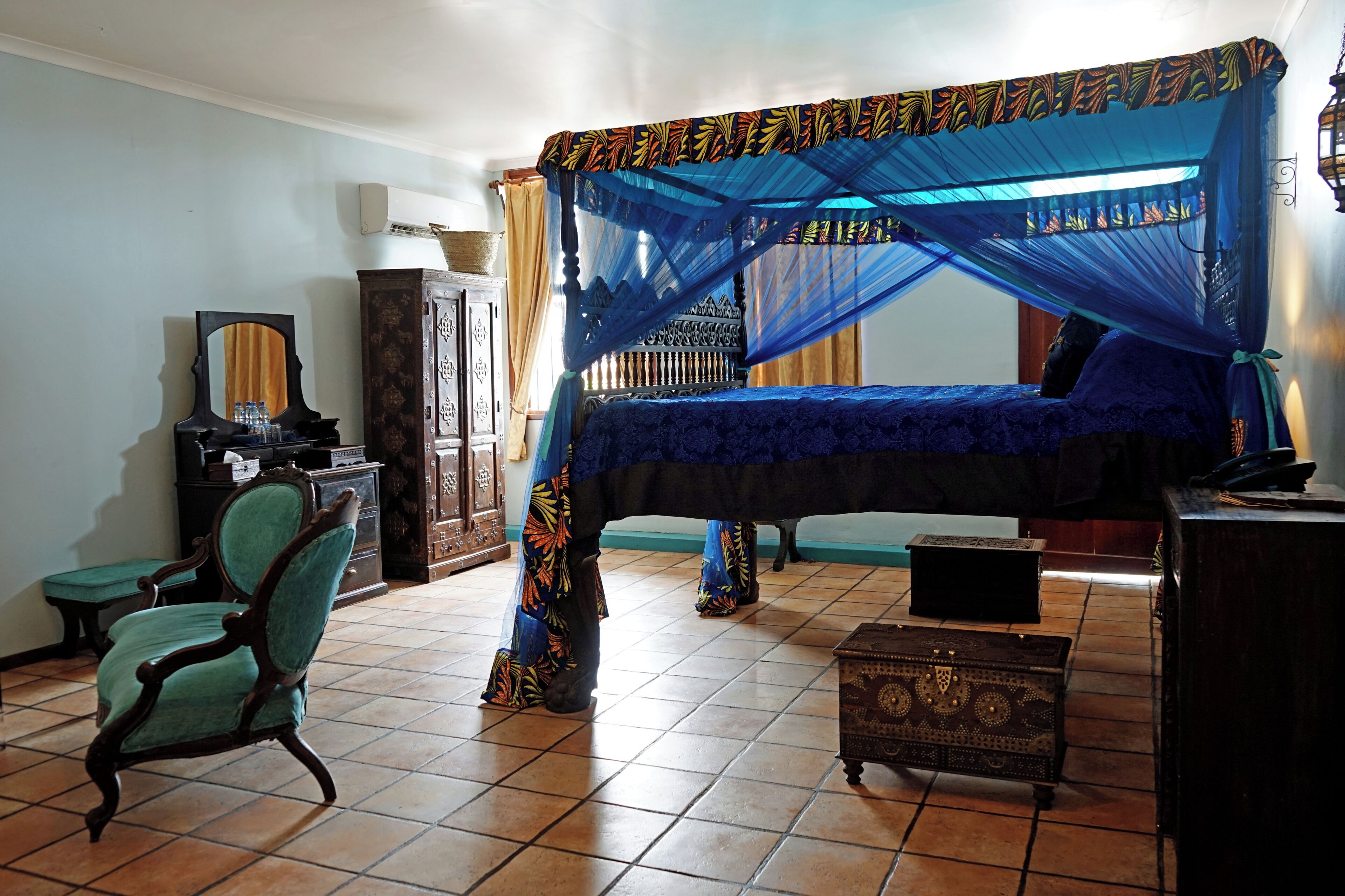 A bedroom with a bed under a blue canopy, a wooden cabinet, a chair, and a small table.