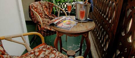 A wicker chair with a floral cushion, a small wooden table with a magazine, and two glasses of a pink beverage.