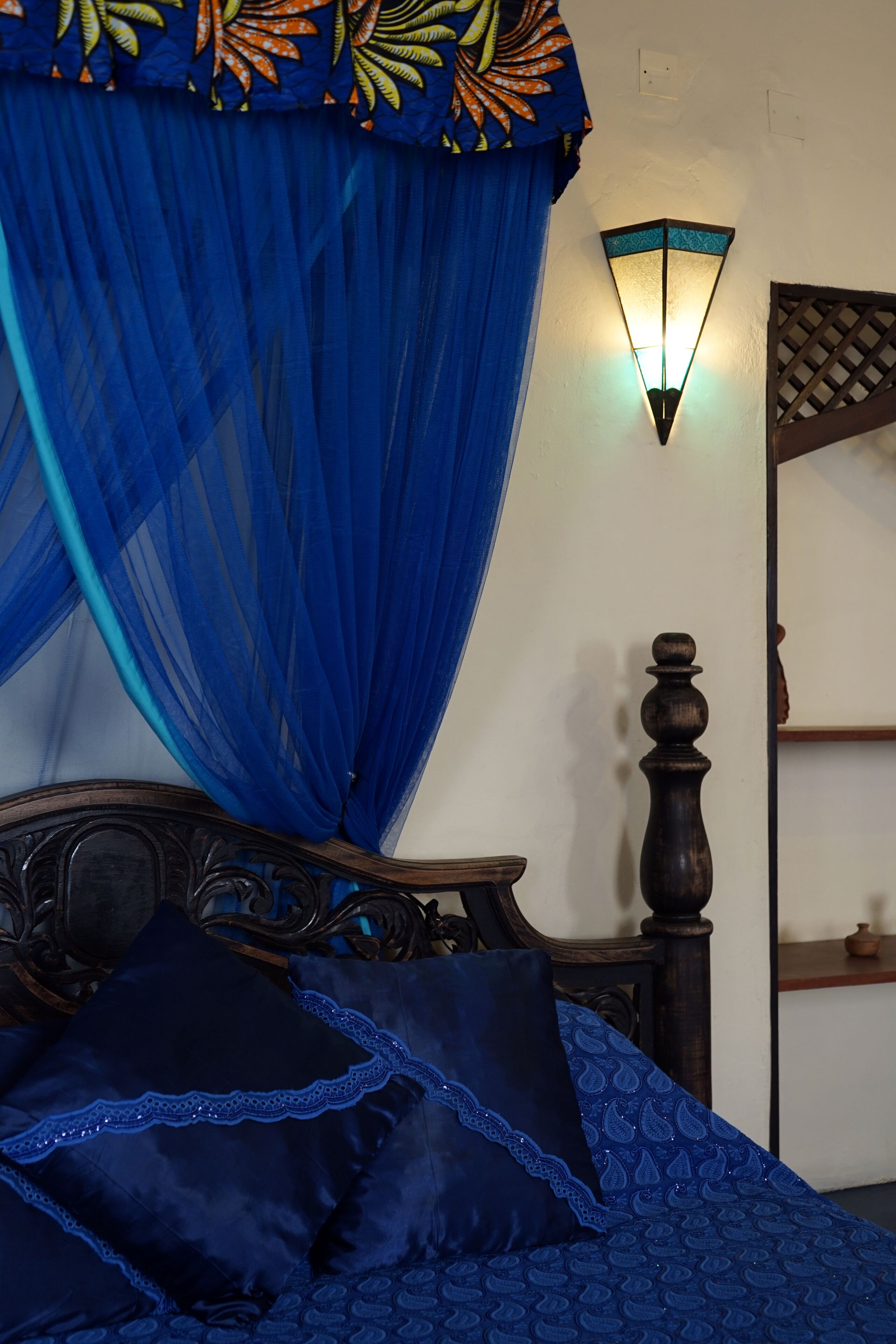 Un lit à baldaquin, un luminaire fixé au mur et une table de chevet en bois.