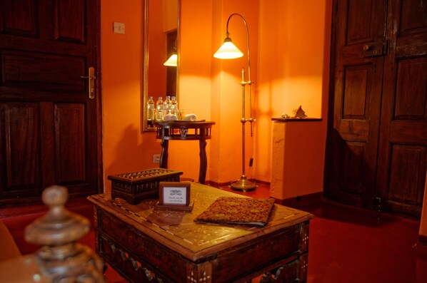 Une pièce avec une table en bois, une lampe, un miroir et une petite étagère où sont posées des bouteilles.