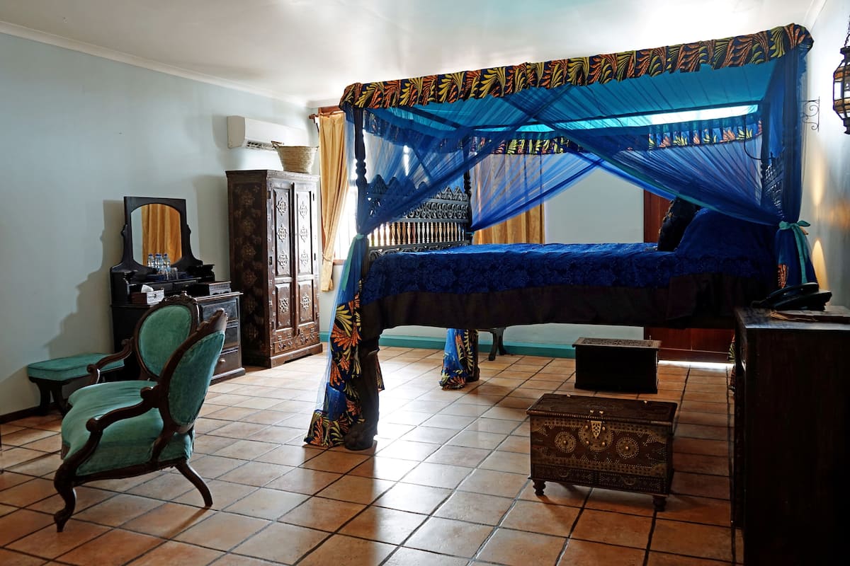 Un dormitorio con una cama bajo un dosel azul, un armario de madera, una silla y una mesita.