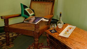 Una sedia di legno con schienale intrecciato, un libro, una bottiglia di liquore e un piatto con cibo su un tavolo di legno.