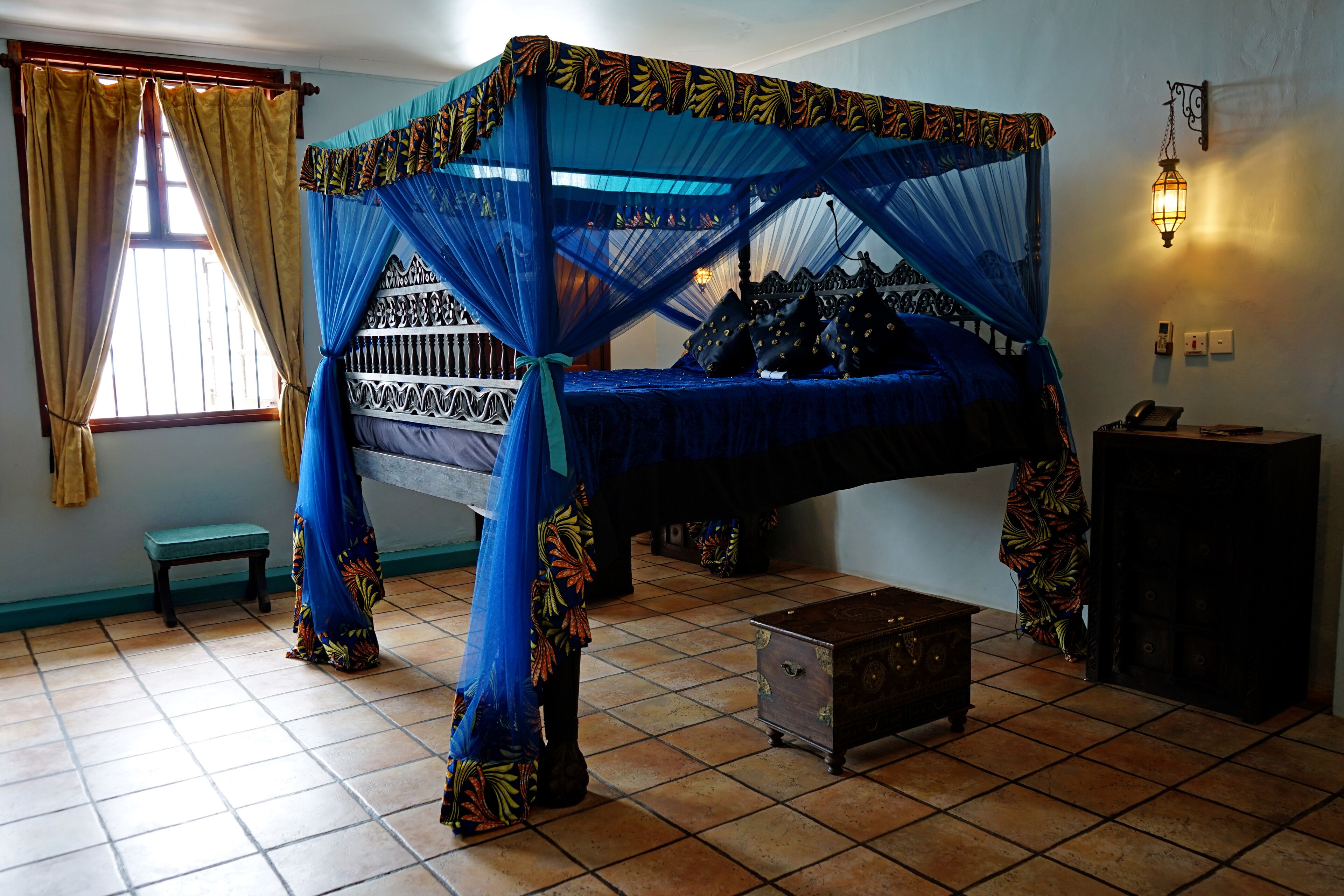 A room with a four-poster bed, a small wooden chest, and a bench.