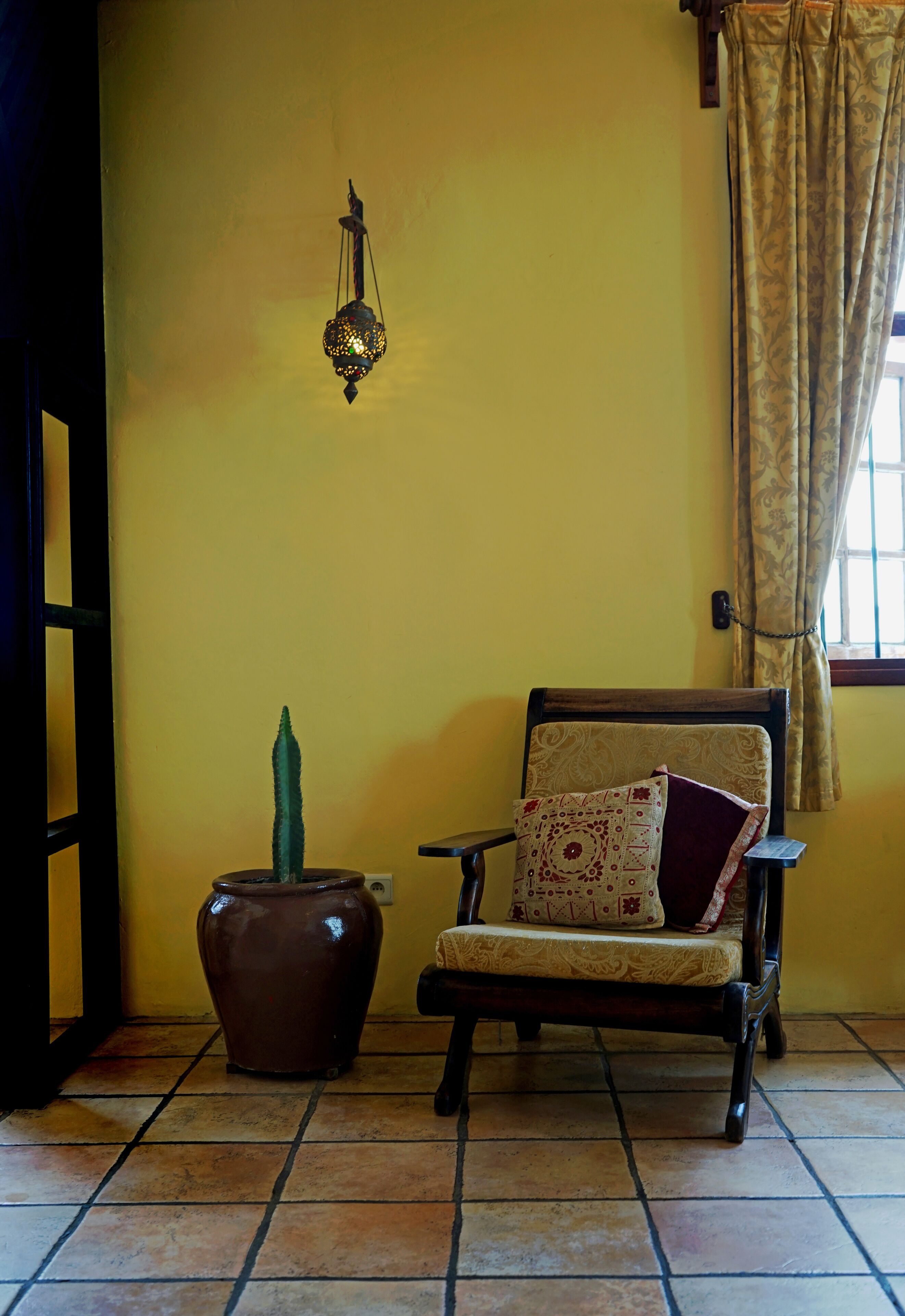 A room with a chair, a potted plant, and a wall-mounted light fixture.
