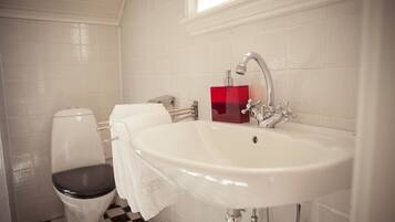 A bathroom with a white sink, a red soap dispenser, a toilet, and a checkered floor.