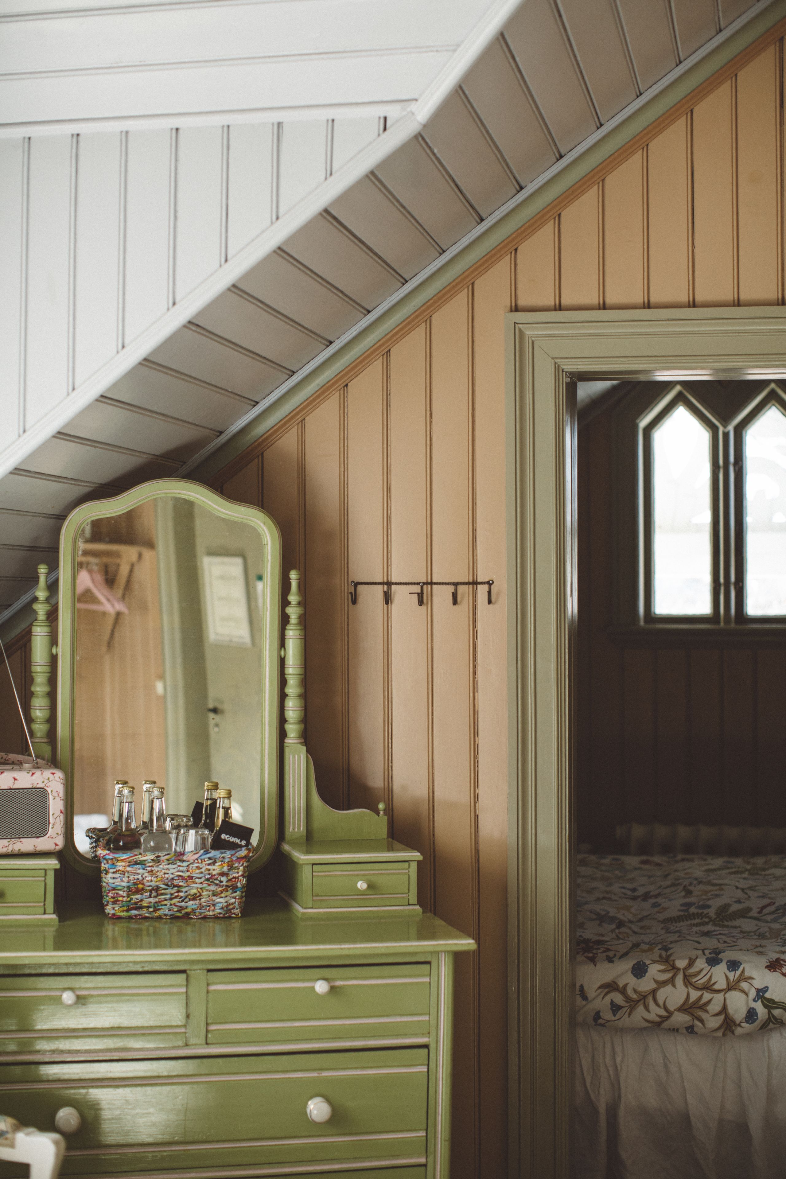 Una habitación con un aparador verde, un espejo y una cama con colcha estampada.