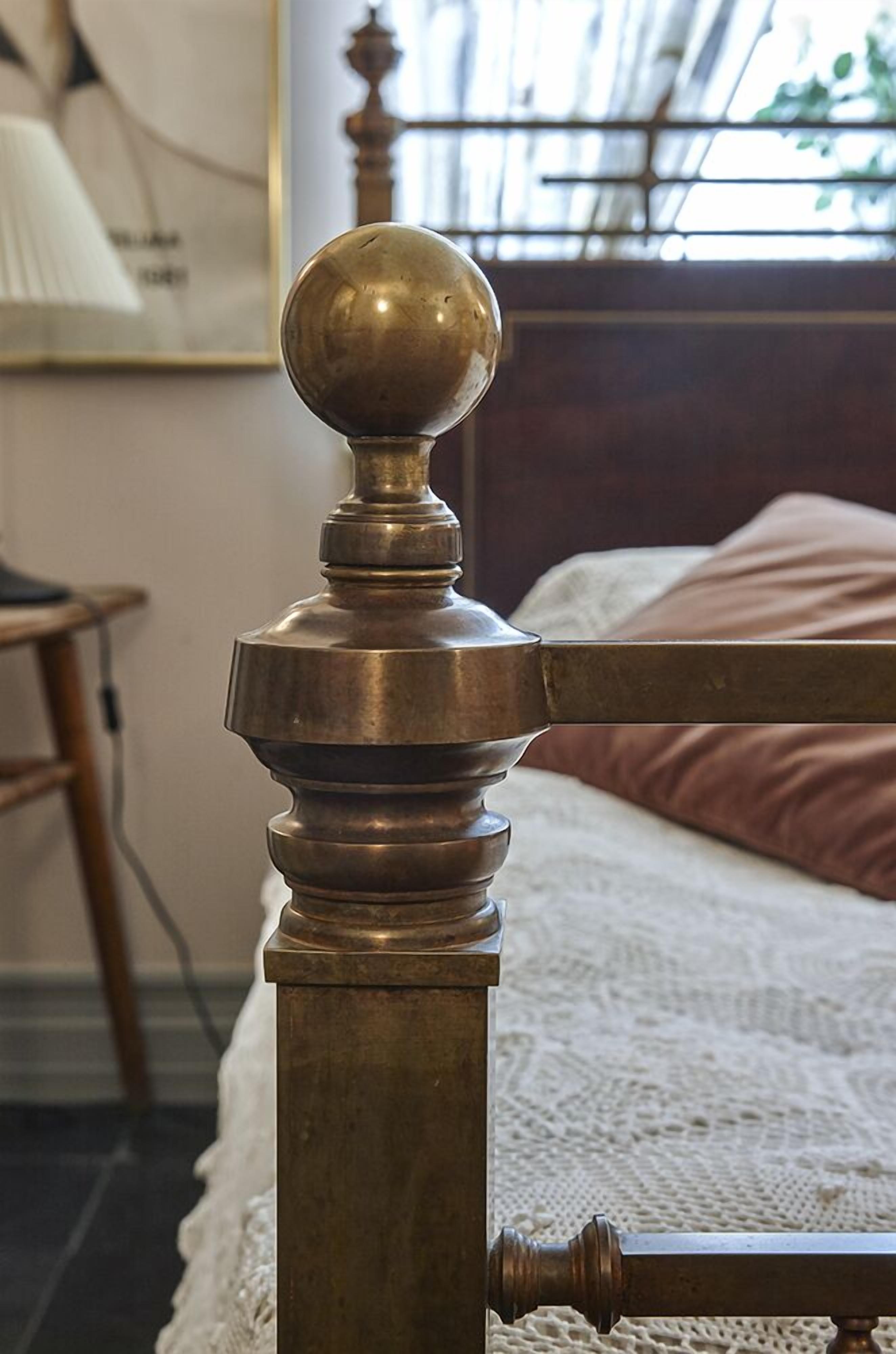 A brass bedpost with a round finial, a wooden headboard, and a white bedspread.