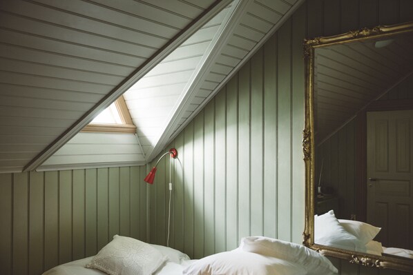Un dormitorio con techo inclinado, un espejo grande y una cama con almohadas.
