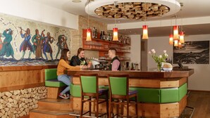 A bar area with wooden bar stools, a mural on the wall, and a wooden ceiling. - Almfrieden (Ramsau am Dachstein)