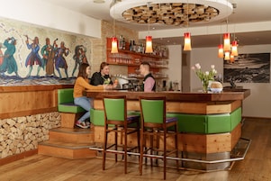 Una zona de bar con taburetes de madera, un mural en la pared y techo de madera.