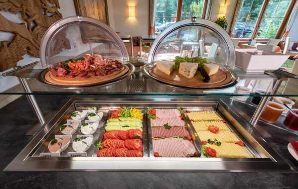 A buffet with various food items and a glass display case. - Almfrieden (Ramsau am Dachstein)