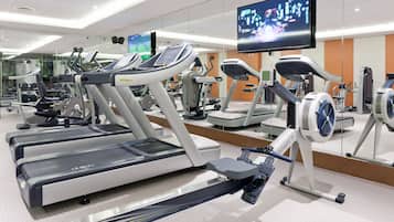 Une salle de sport équipée de plusieurs tapis de course, de vélos d’exercice et d’un écran de télévision diffusant un événement sportif.