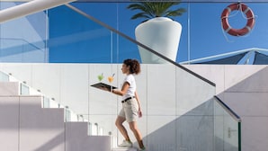 A person descending a modern staircase with glass railings and a large potted plant in the background.