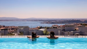 A swimming pool with two people in the water, overlooking a cityscape and a body of water.