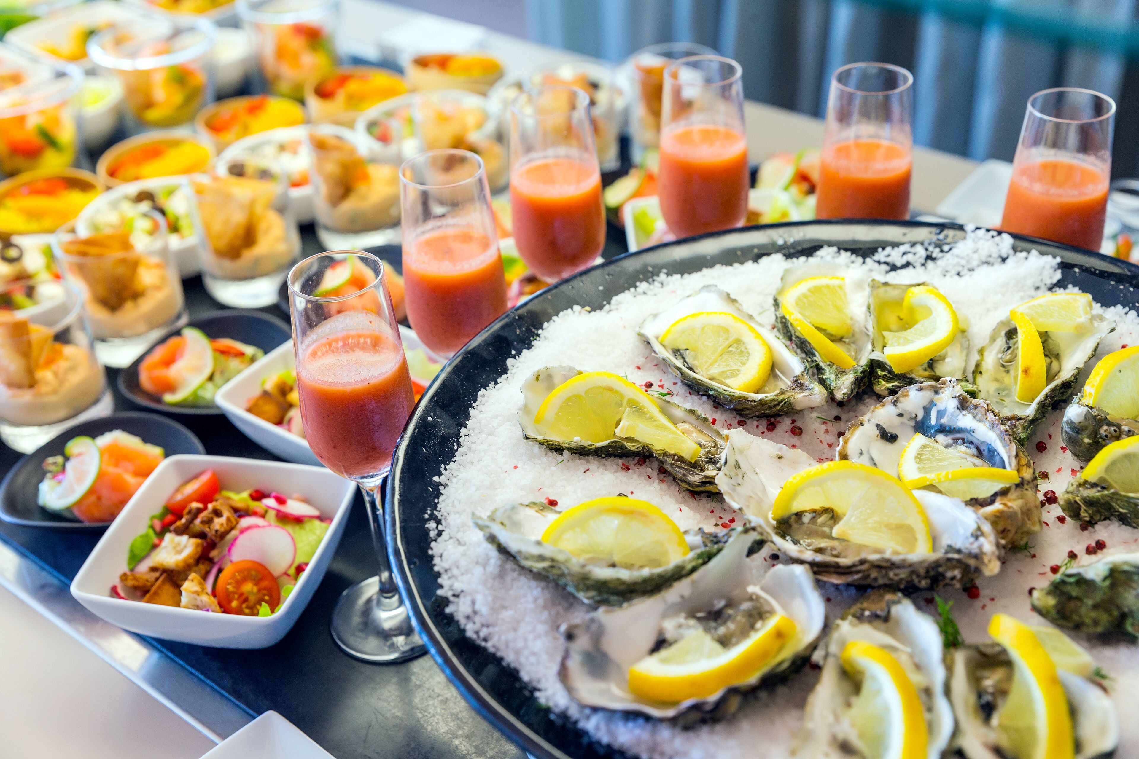 Variedad de platos de mariscos, incluyendo ostras sobre hielo con rodajas de limón, y varios pequeños cuencos de ensalada y otras entradas.