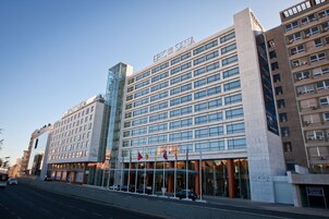 A multi-story hotel with a modern facade, large windows, and a prominent entrance with flags.