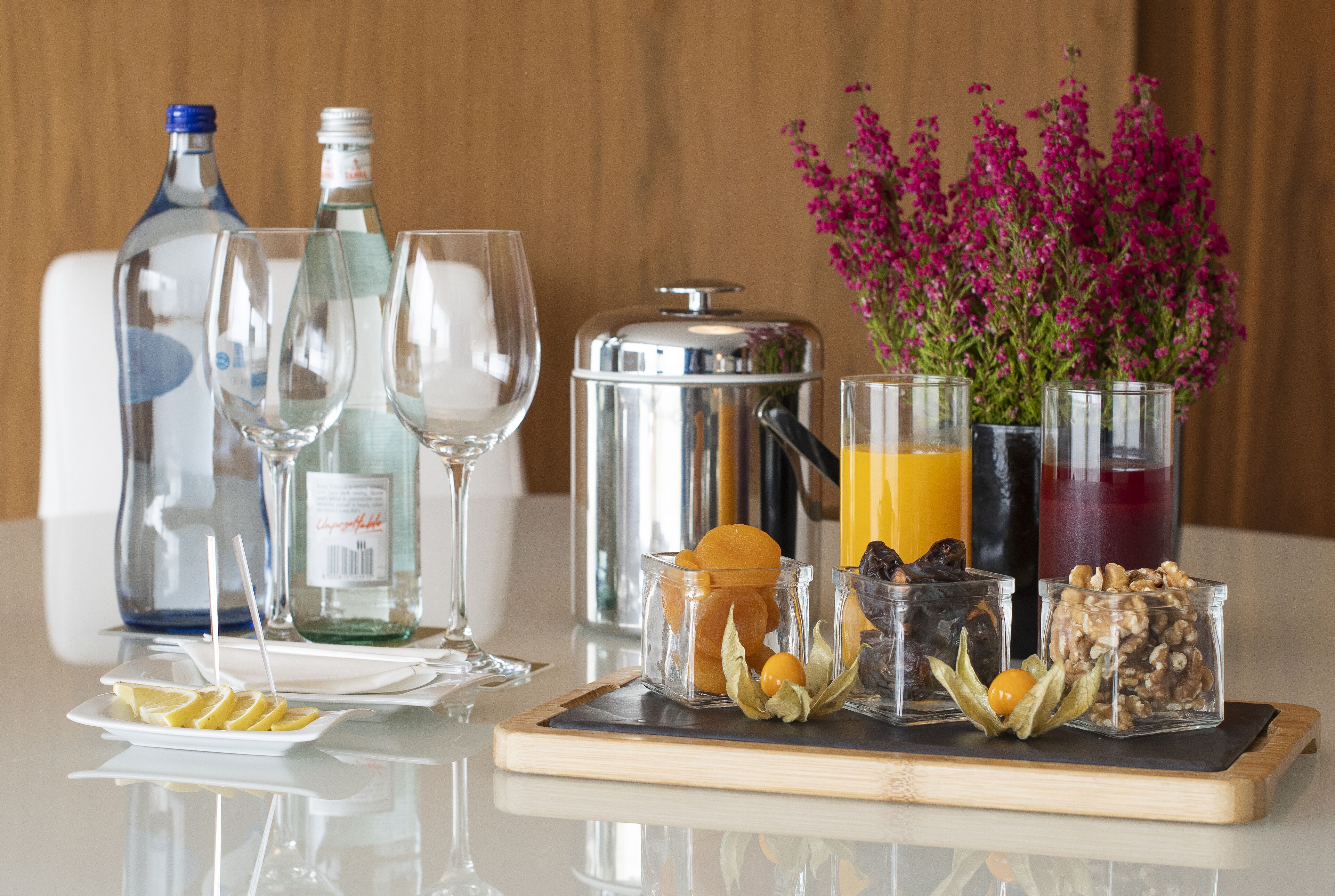 A breakfast tray with beverages, a bottle of water, a glass of wine, and a plate of lemon slices.