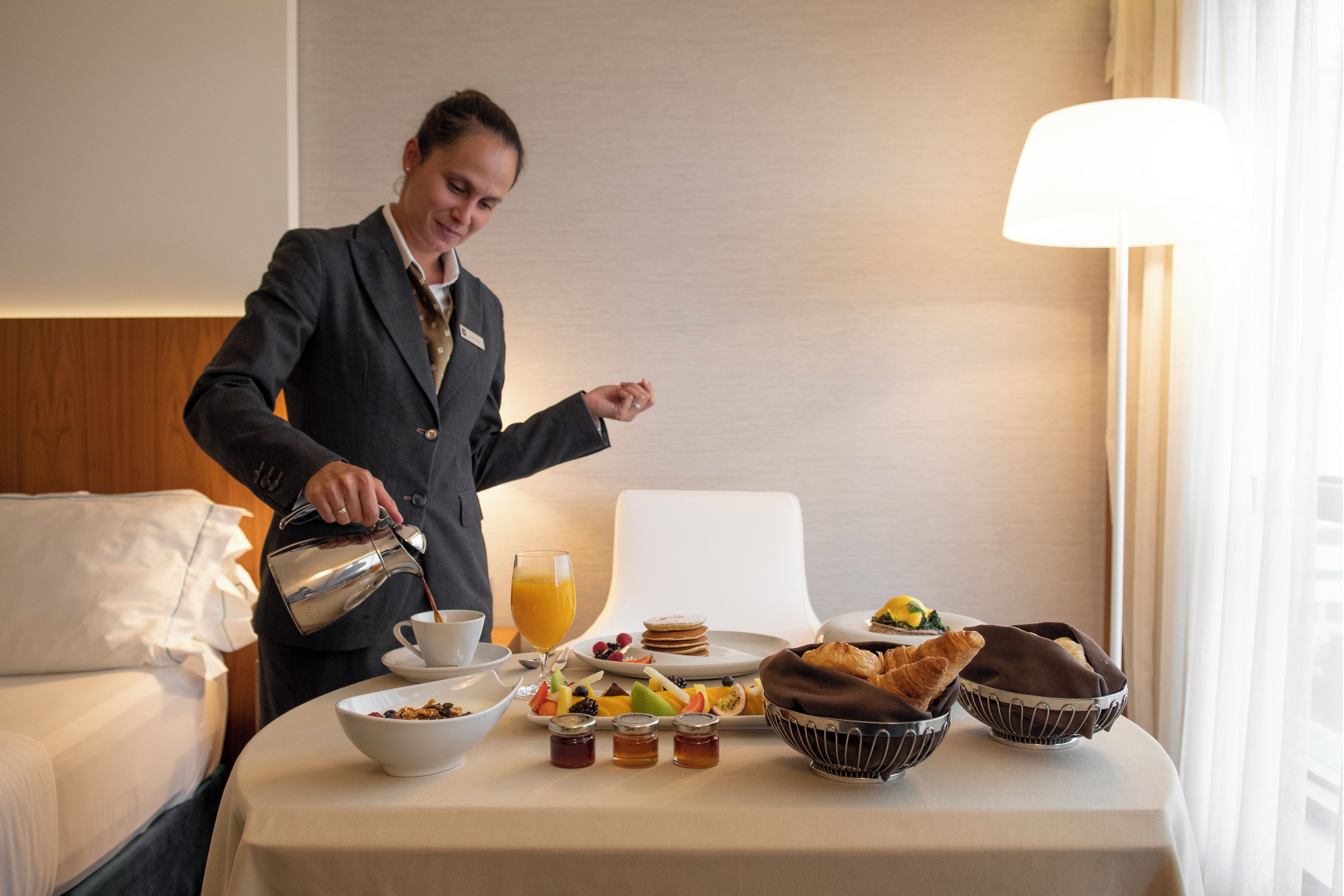 A hotel room with a breakfast setup including a coffee pot, a glass of orange juice, and various breakfast items on the table.