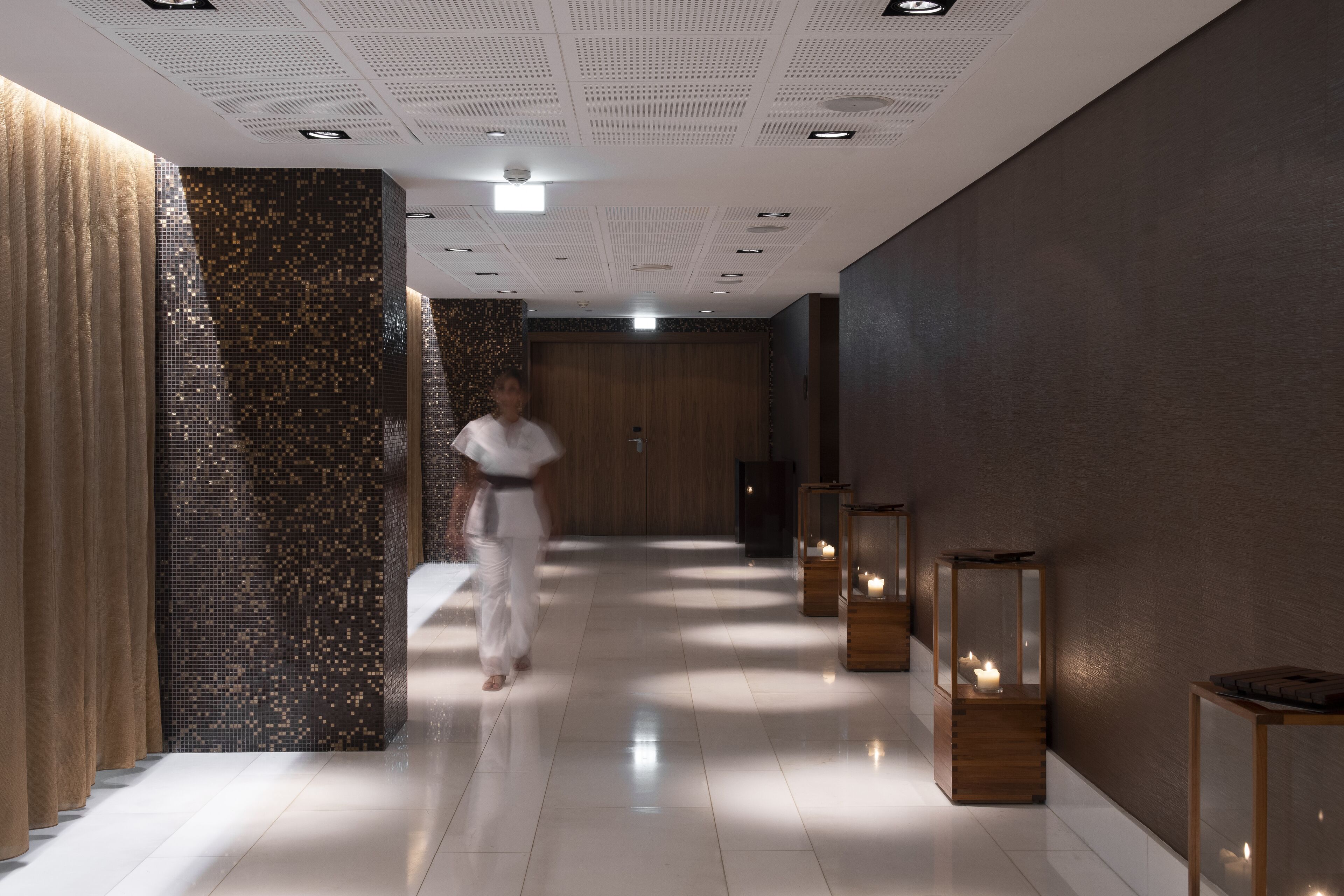 A modern hallway with a reflective floor, a person walking, and decorative lighting fixtures.