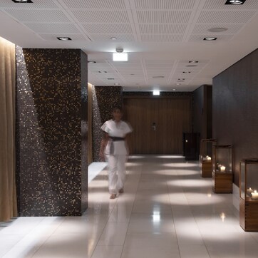 A modern hallway with a reflective floor, a person walking, and decorative lighting fixtures.