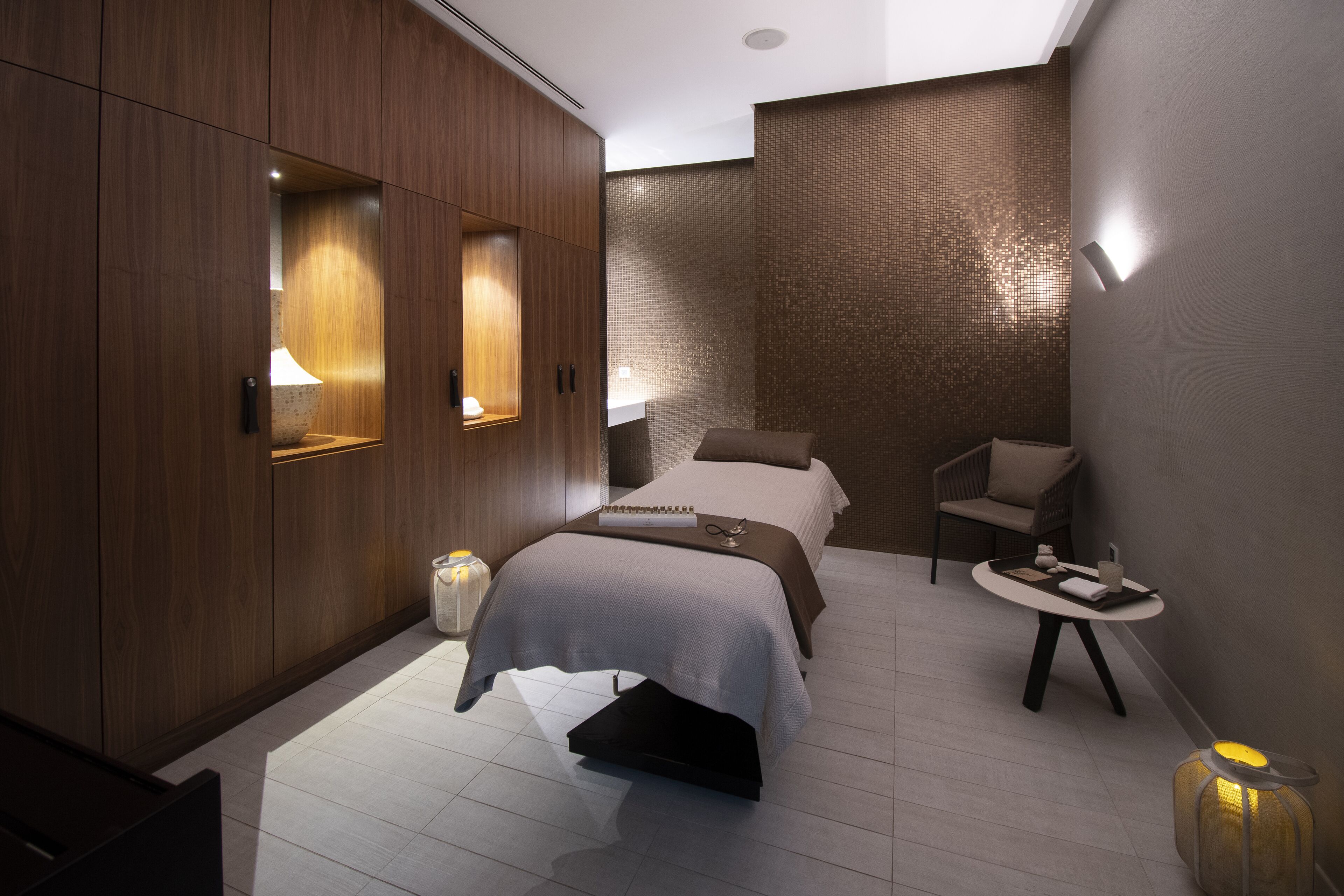 A modern hotel room with a large bed, a small table, a chair, and a decorative floor lamp.