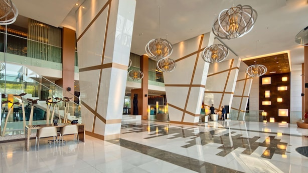A spacious lobby with modern chandeliers, a glass staircase, and a seating area.