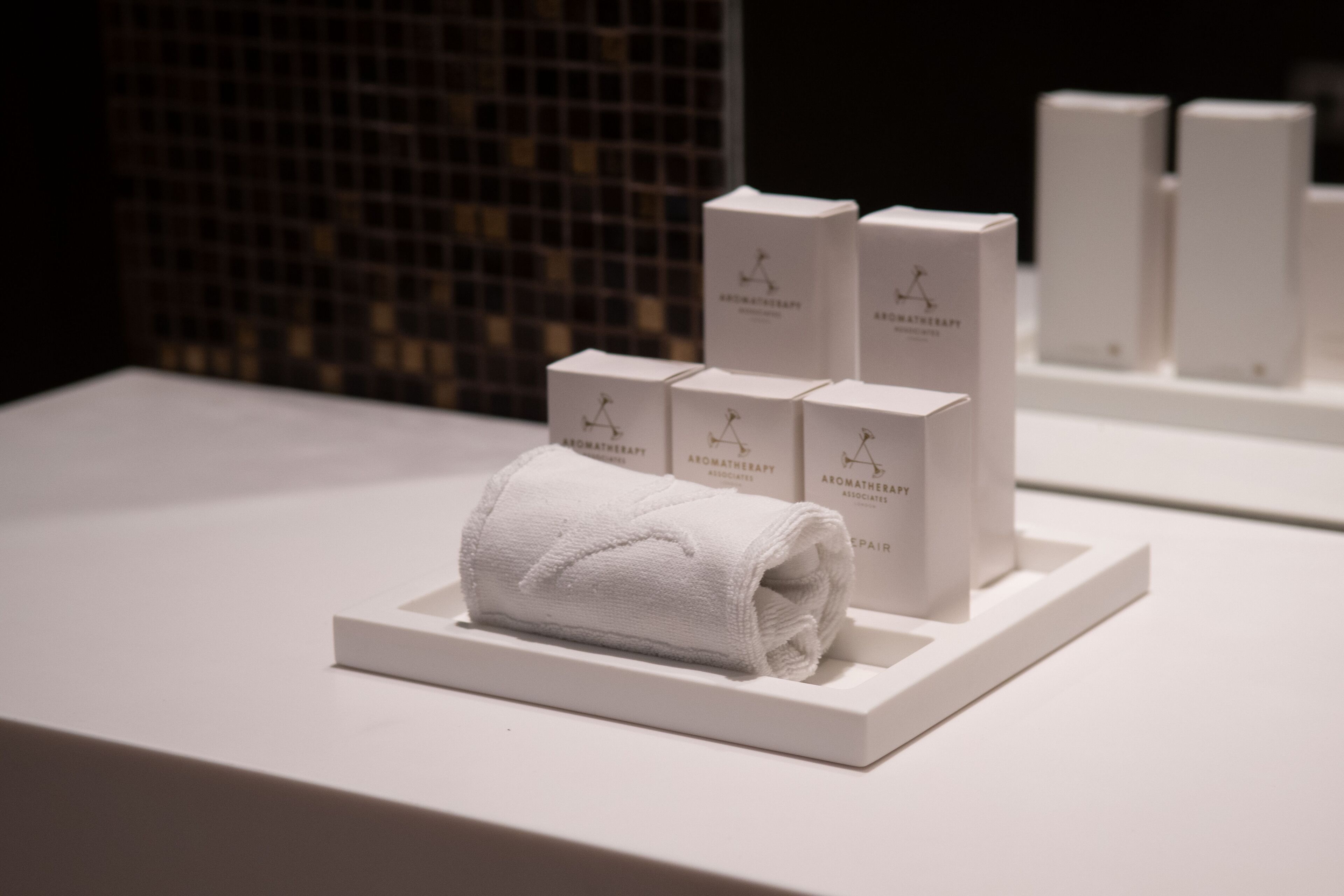 A neatly arranged display of white boxes and a rolled white towel on a white platform, likely in a hotel or spa setting.