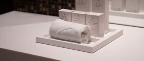 Una presentación ordenada de cajas blancas y una toalla blanca enrollada sobre una plataforma, probablemente en un hotel o spa.