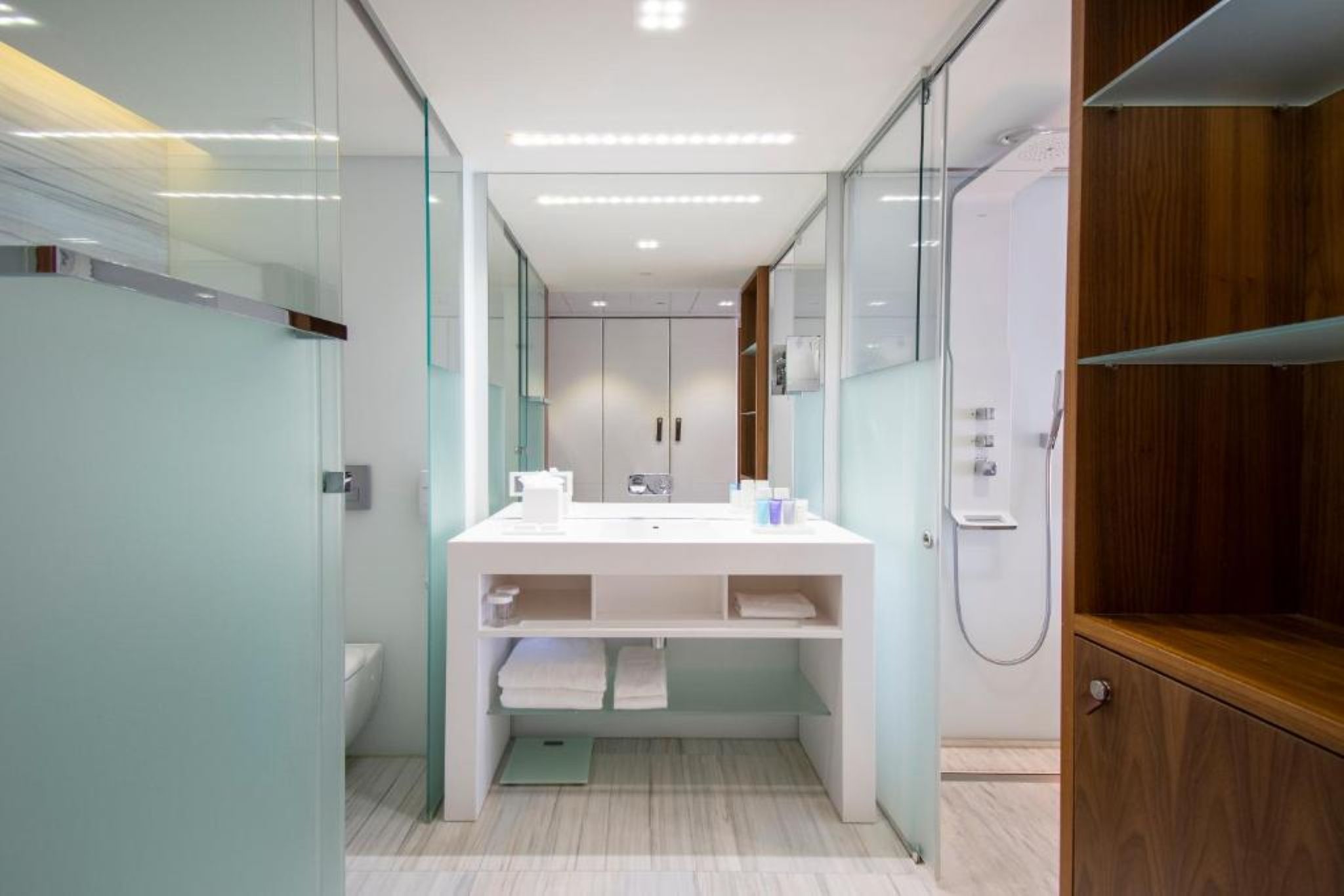 A modern bathroom with a glass partition, a white vanity, and a wooden cabinet.