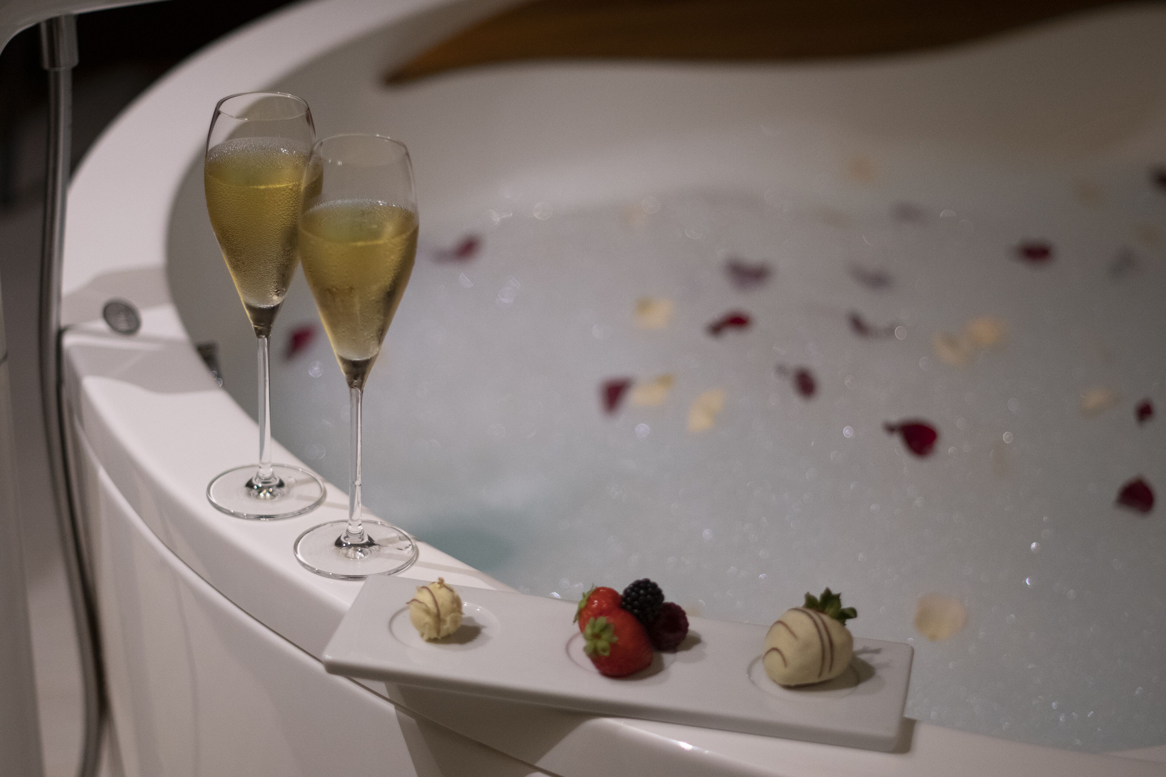 A bathtub with champagne glasses and fruit.