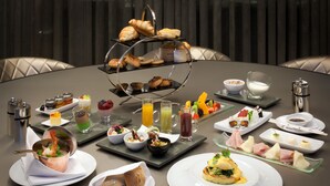 A breakfast buffet with various dishes, drinks, and pastries on a round table.