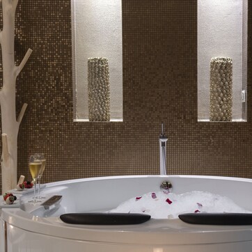 A modern bathroom with a freestanding bathtub, a wooden bath mat, and a glass of champagne.