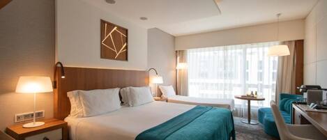 A hotel room with a large bed, a desk, a chair, and a window with curtains.