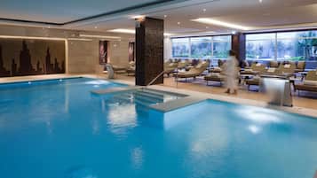 A modern indoor pool area with a clear water surface, a central column, and lounge chairs arranged around the pool.