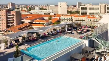 A rooftop pool with lounge areas, a glass balustrade, and a cityscape view.