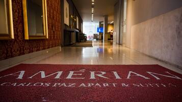 Un hall de hotel con alfombra roja que reza "AMÉRIAN" y "CARLOS PAZ APART & SUITES".
