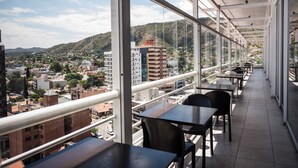 Un balcón con mesas y sillas, con vistas a un paisaje urbano y colinas.