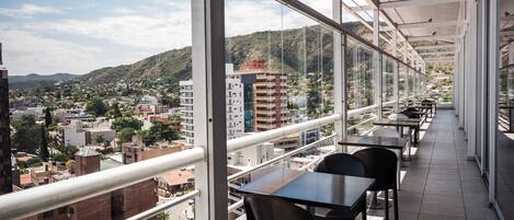 Un balcón con mesas y sillas, con vistas a un paisaje urbano y colinas.