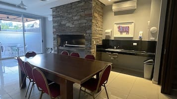 Una cocina moderna con una pared de acento de piedra, un comedor con una mesa grande y sillas rojas, y vistas a un patio exterior a través de un vidrio.