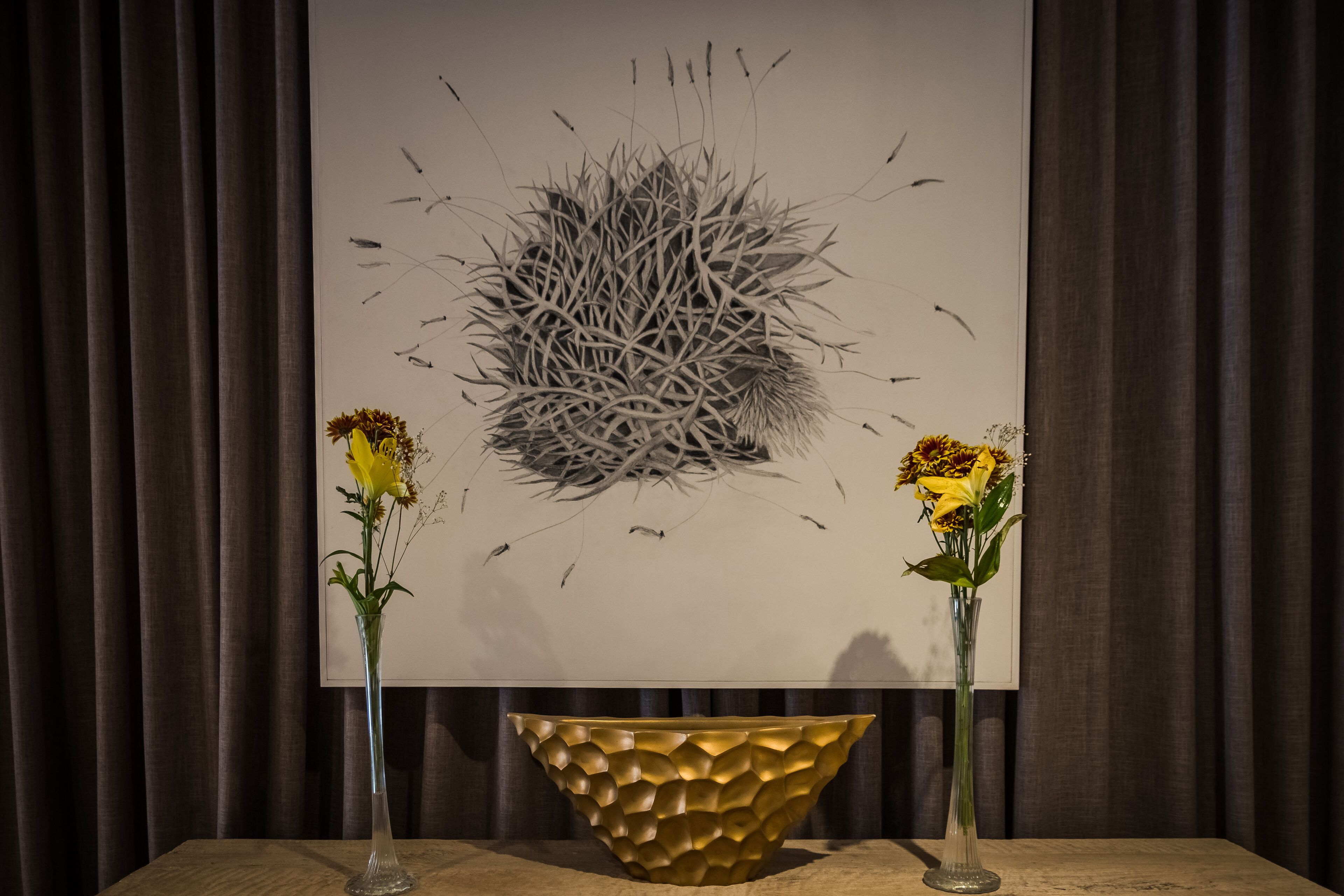 Una habitación con un cuadro abstracto grande en la pared, un cuenco dorado sobre una mesa y dos jarrones con flores amarillas.
