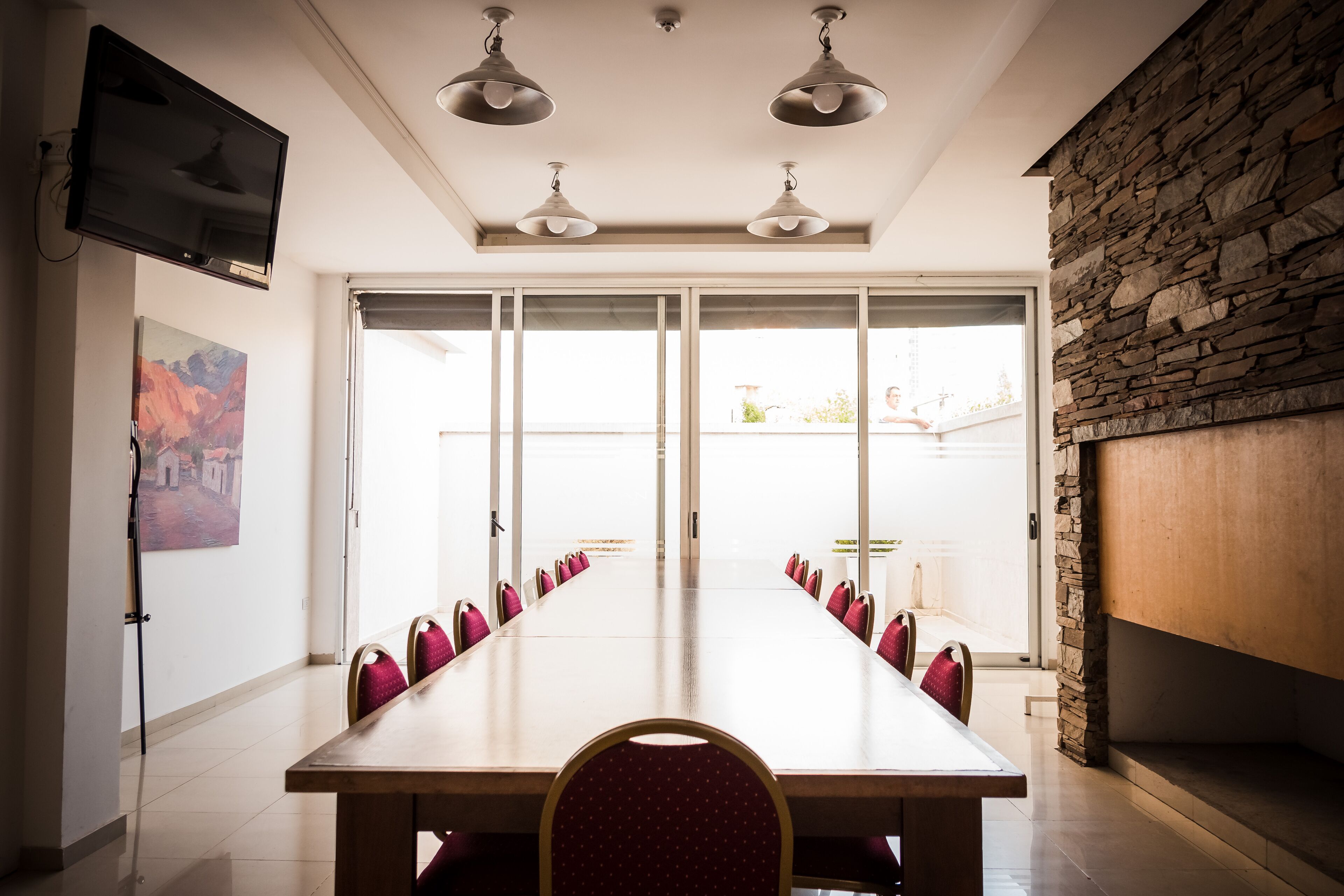 Un salón de conferencias con una mesa larga, sillas, un televisor y una pared de piedra.