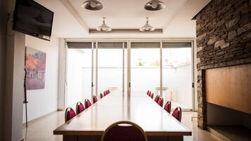 Un salón de conferencias con una mesa larga, sillas, un televisor y una pared de piedra.