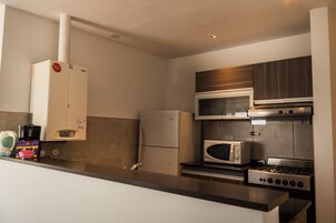 Una cocina compacta equipada con refrigerador, microondas, estufa y cafetera.